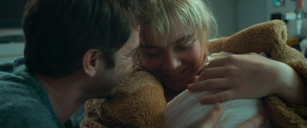 A close-up shot of Alumt (Florence Pugh) and Tobias (Andrew Garfield) embracing a teddy bear together in an intimate moment, captured with soft, cool-toned lighting in the feature 